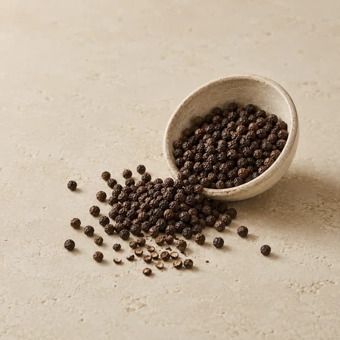 Black peppercorns spilling from a ceramic bowl